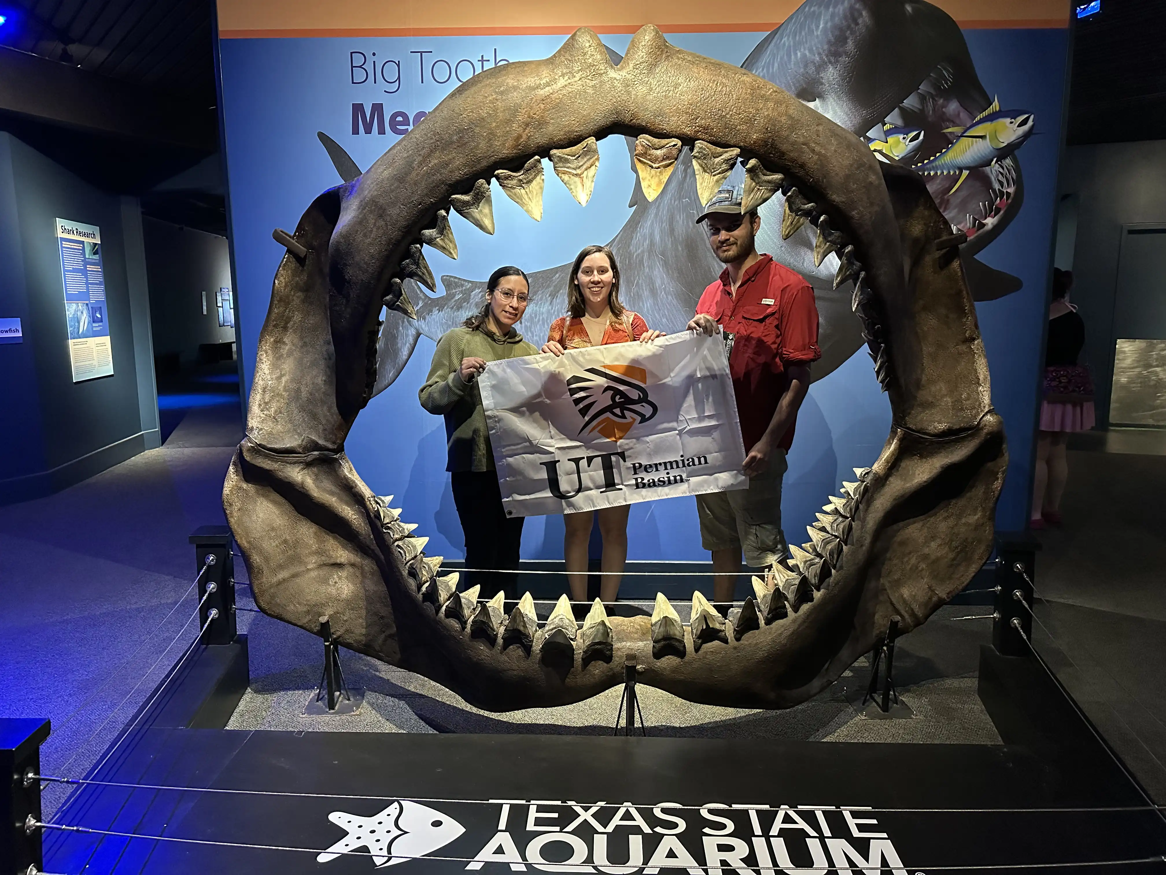 UTPB oceanography students posed with a UTPB flag at the Texas State Aquarium inside a shark's mouth
