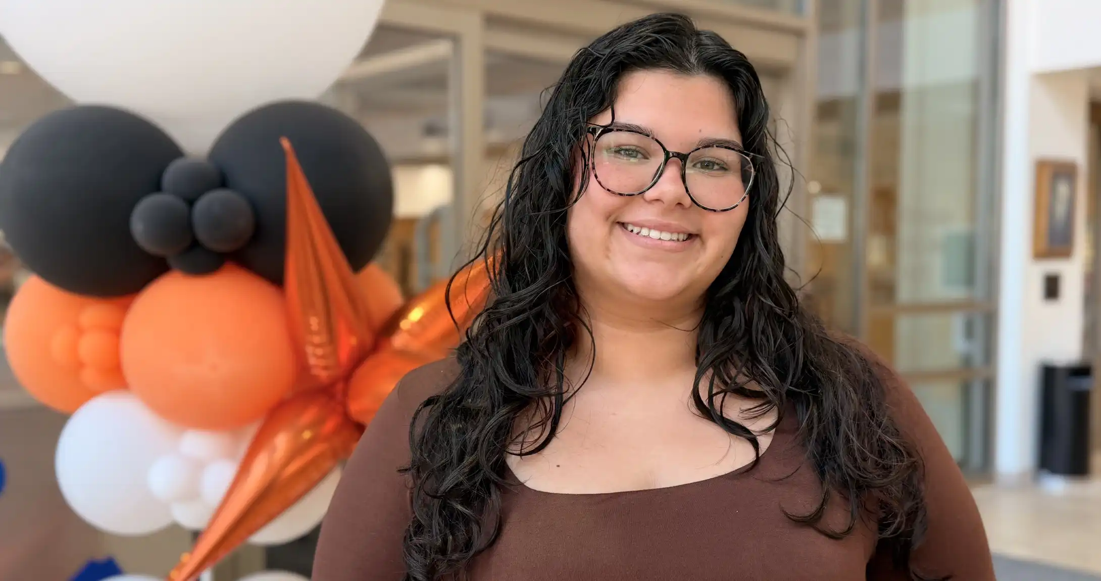 Alanis Lopez standing in the on campus library in front of UTPB balloons. 
