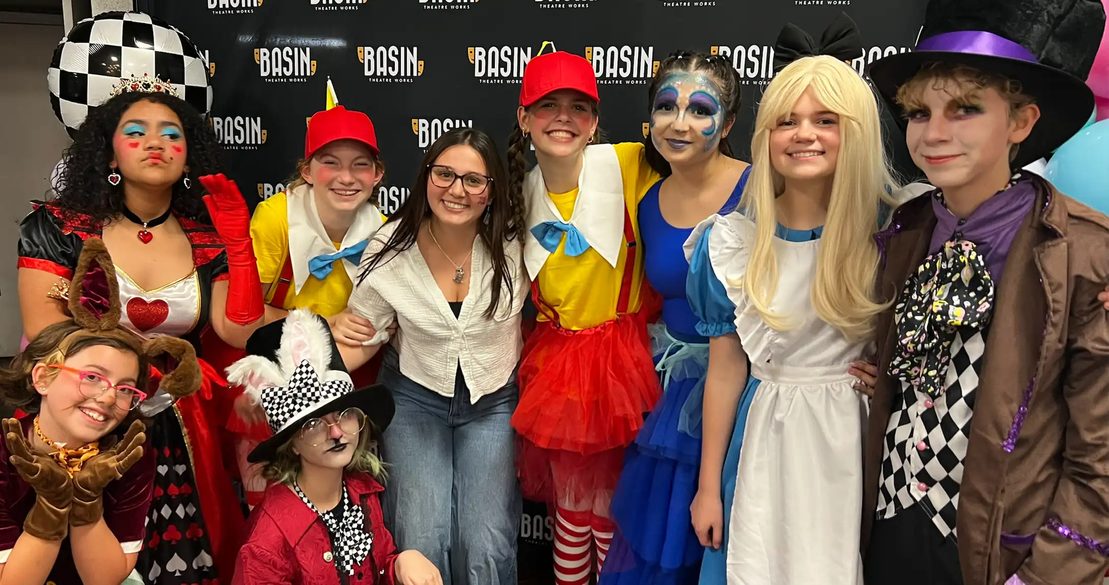 A photo of Ameri Clark with a group of campers posing for a photo at the end of their performance of Alice in Wonderland Jr.