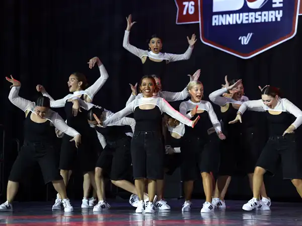A group of dancers from UTPB in formation in the back corner of the stage with their arms up and someone in the center posing. 