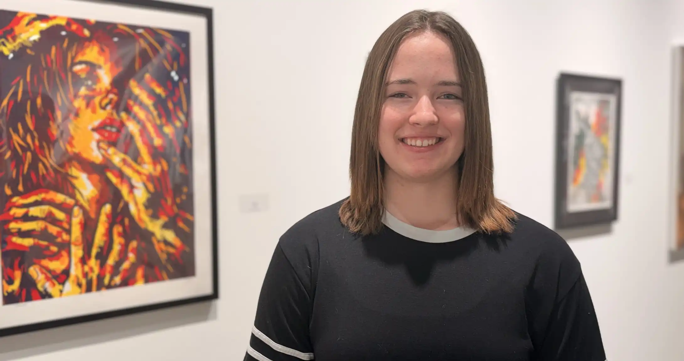 Riley Miller standing in front of her art work displayed on campus.