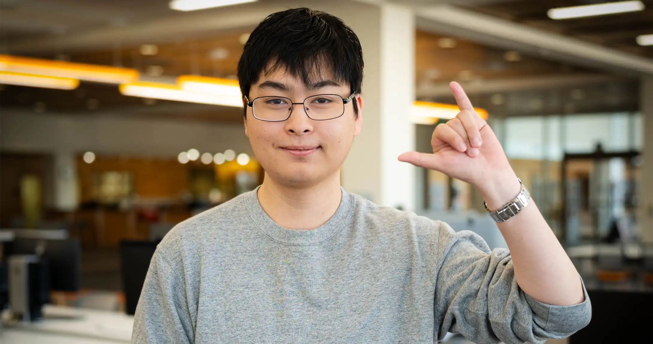 Panhapiseth Lim standing in the library while holding his Falcons Up hand sign. 