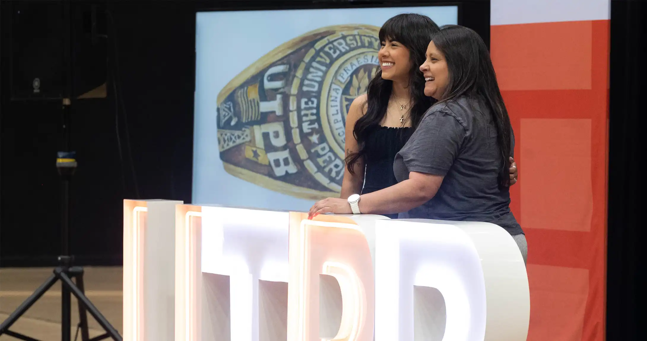 A photo of a UTPB student posing for a photo with her mom behind UTPB marquee letters at the ring ceremony.