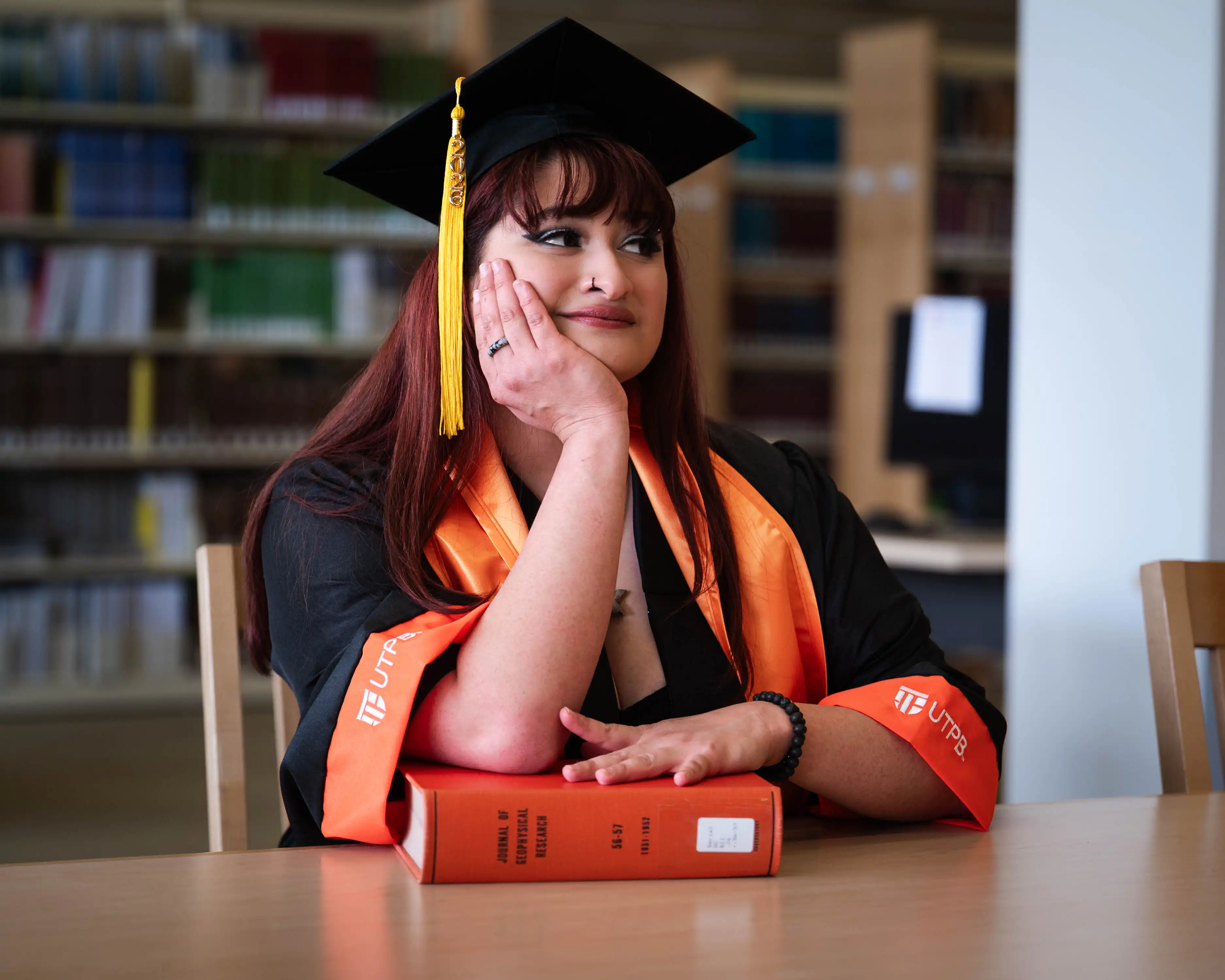 RosaAliyah Olguin sitting with her elbow propped on a book in the UTPB library. 