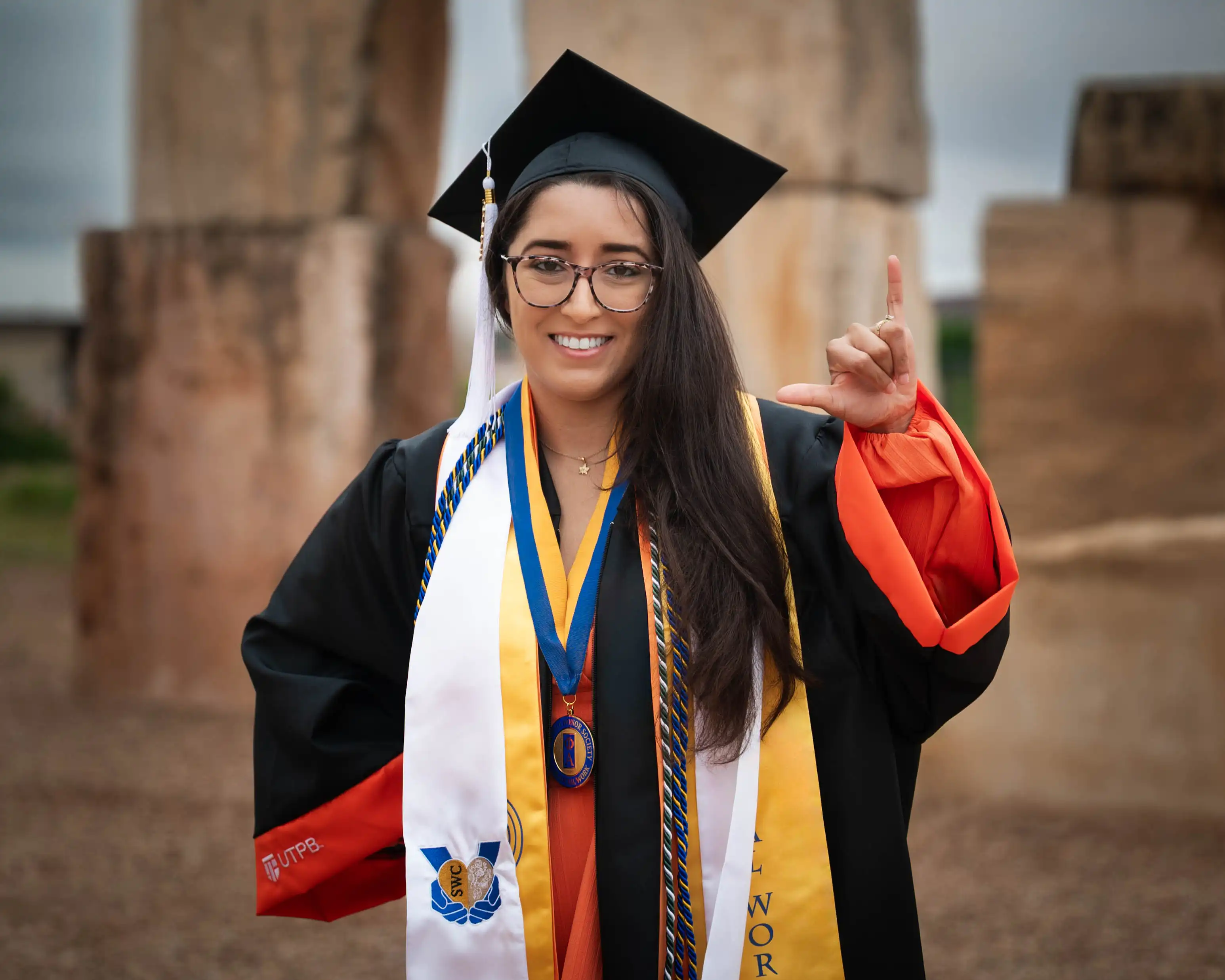 Valarie James in her graduation regalia standing at the UTPB Stonehenge Replica. 